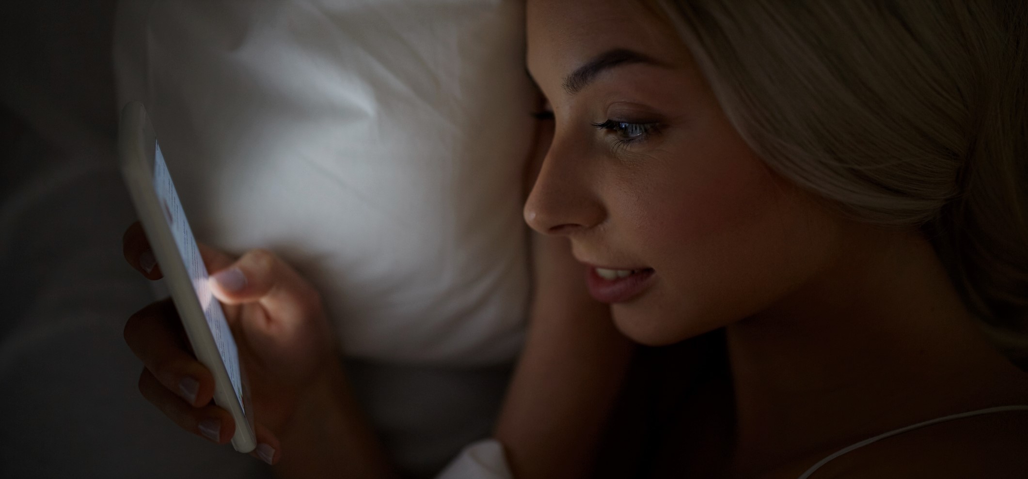 technology, internet, communication and people concept - happy smiling young woman texting on smartphone in bed at home bedroom at night