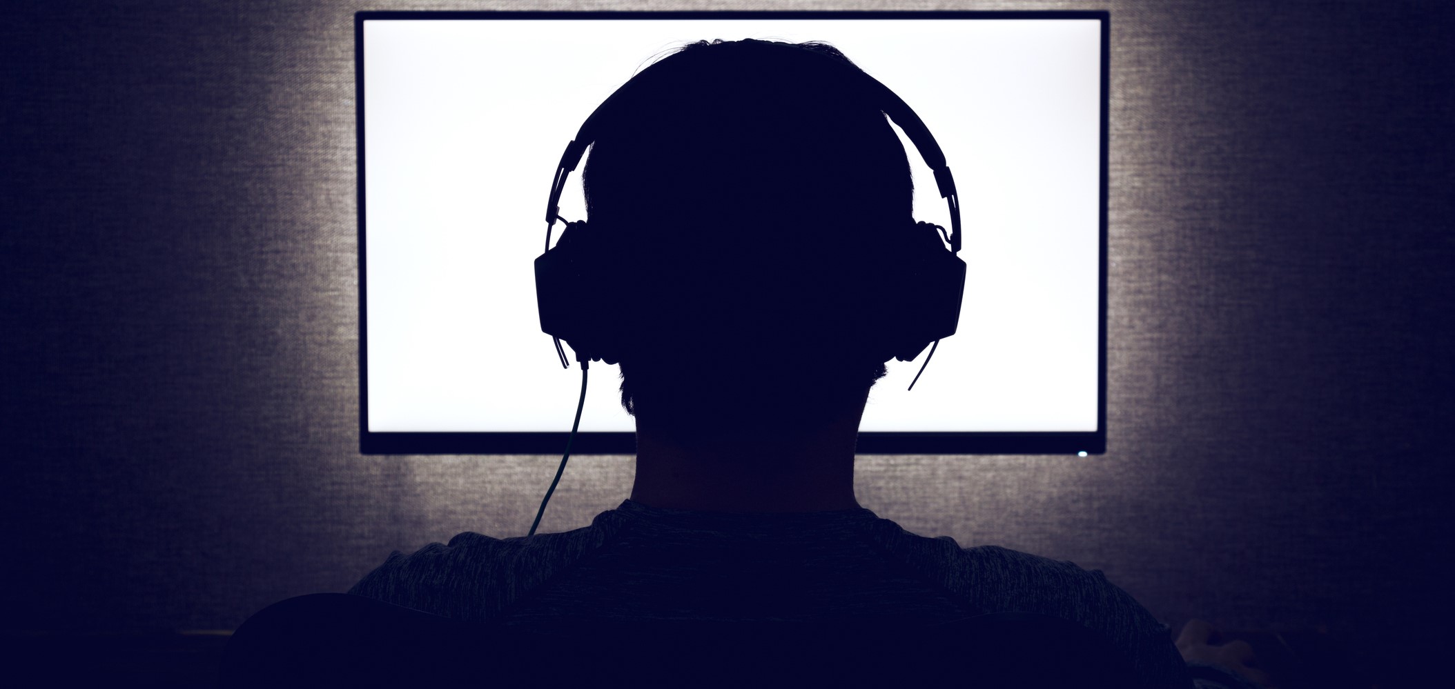 Man in headphones sits in front of a blank monitor in dark room
