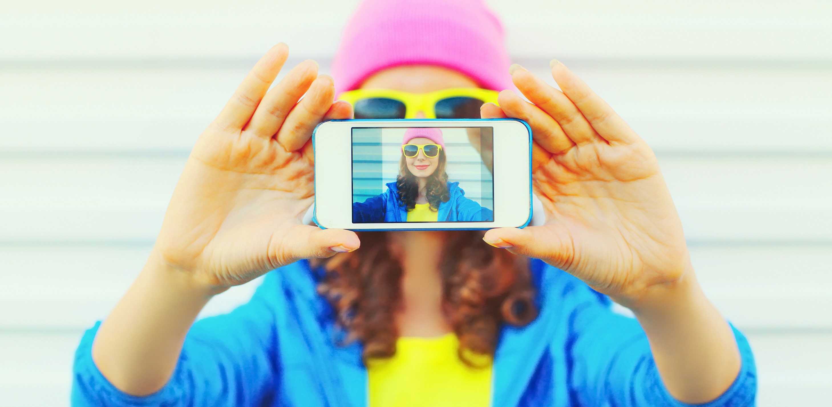 Fashion pretty cool girl taking photo self portrait on smartphone over white background wearing colorful clothes and sunglasses